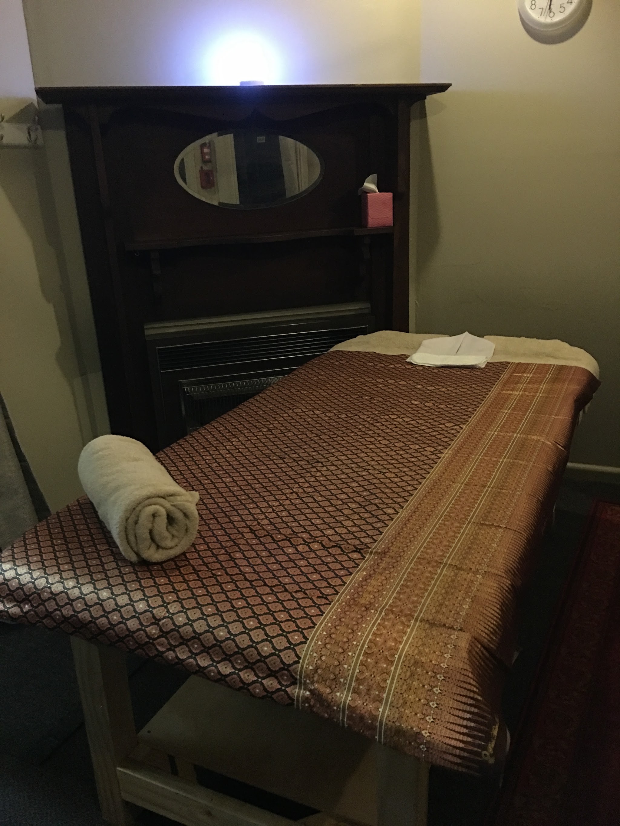 A treatment room with a Thai-pattern cover on the massage table and a rolled towel