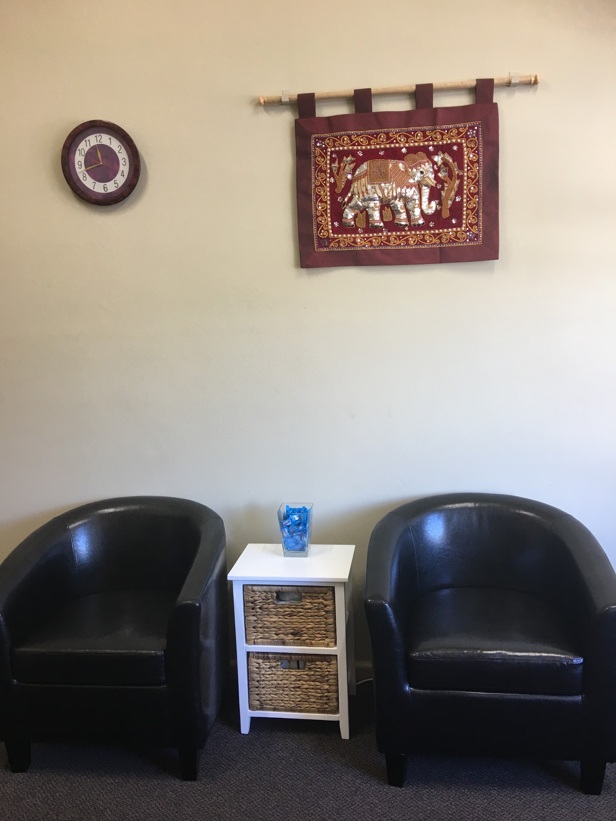 The waiting area with two leather tub chairs and a framed Thai elephant tapestry