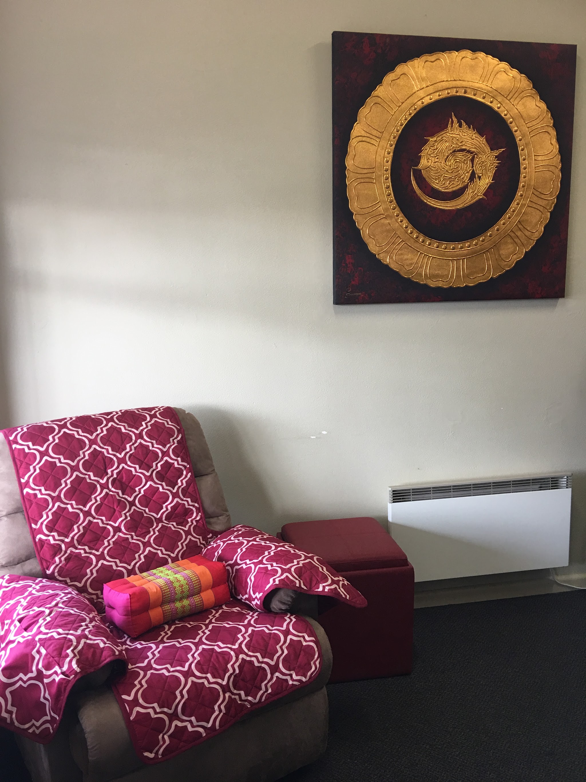 A reclining chair with a magenta throw and a Thai triangle cushion beneath a gold Thai wall artwork